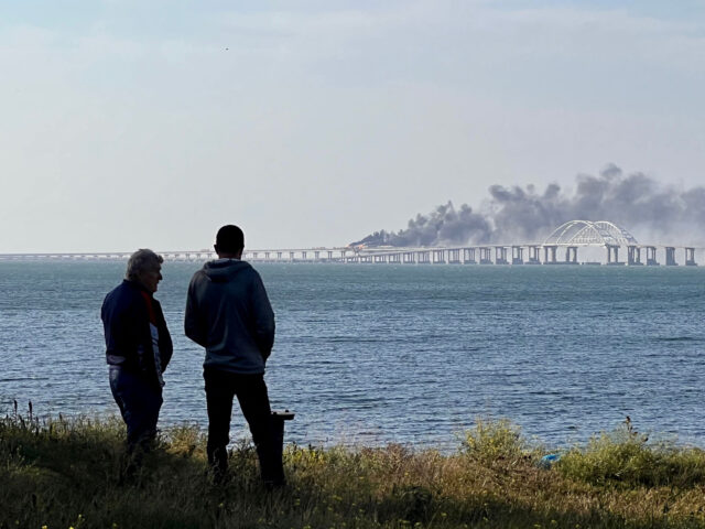 People look at thick black smoke rising from a fire on the Kerch bridge that links Crimea to Russia, after a truck exploded, near Kerch, on October 8, 2022. - Moscow announced on October 8, 2022 that a truck exploded igniting a huge fire and damaging the key Kerch bridge …