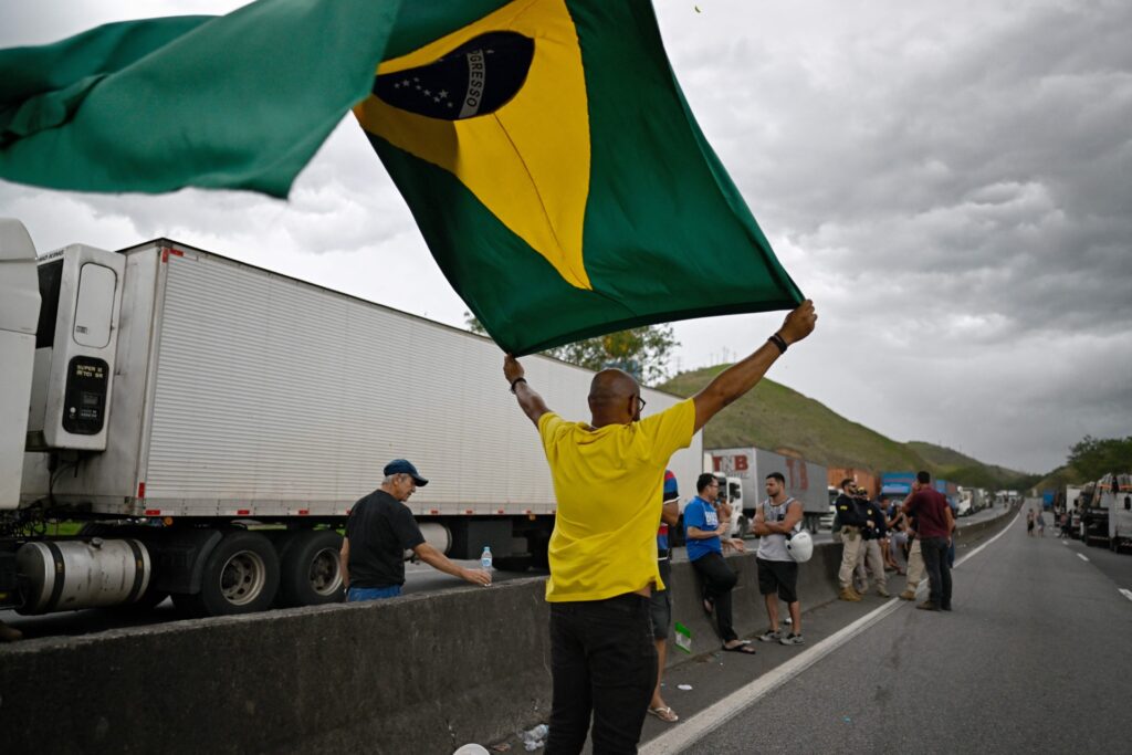 A supporter of President Jair Bolsonaro holds a Brazilian national flag during a blockade on the Via Dutra BR-116 highway between Rio de Janeiro and Sao Paulo, in Barra Mansa in the Brazilian state of Rio de Janeiro, on October 31, 2022, as an apparent protest by mainly truck drivers over Bolsonaro's defeat in the presidential run-off election. - Truckers and other protesters on Monday blocked some highways in Brazil in an apparent protest over the electoral defeat of Bolsonaro to leftist Luiz Inacio Lula da Silva, authorities said. (Photo by Mauro PIMENTEL / AFP) (Photo by MAURO PIMENTEL/AFP via Getty Images)