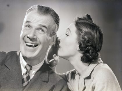 (Original Caption) A man reacts with amusement as a woman whispers in his ear. Undated pho