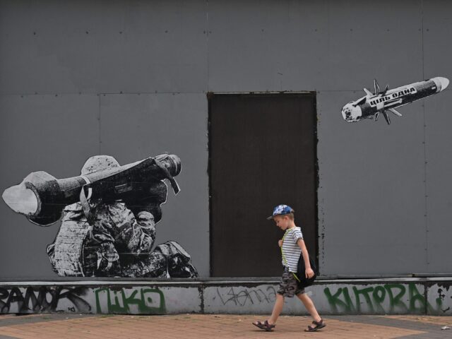 A boy walks past a graffiti on a wall depicting a Ukrainian serviceman making a shot with