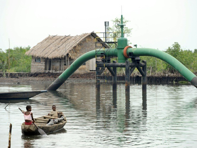 Children sail past an oil pipeline head near their home at Andoni settlement, Bonny waterw