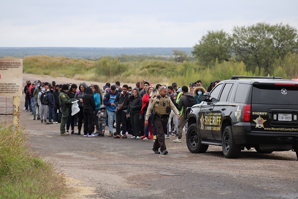 A Texas sheriff's deputy detains a large group of migrants while waiting for Border Patrol near Eagle Pass. (Randy Clark/Breitbart Texas)