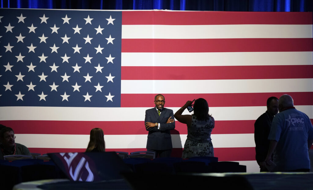 Paris Dennard poses for a photo in front of a U.S. flag before the opening general session of Conservative Political Action Conference (CPAC) Friday, July 9, 2021, in Dallas. (AP Photo/LM Otero)