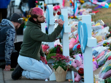 A man signs a cross at a makeshift tribute with a display of bouquets of flowers on a corner near the site of a mass shooting at a gay bar Monday, Nov. 21, 2022, in Colorado Springs, Colo. (AP Photo/Jack Dempsey)