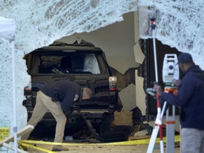 A law enforcement official, center, examines an SUV inside an Apple store, Monday, Nov. 21, 2022, in Hingham, Massachusetts. The crash left a large hole in the glass front of the Apple store. (Steven Senne/AP)