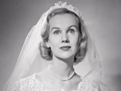 1950s portrait of blonde bride demure expression wearing lace gown veil holding bridal bou
