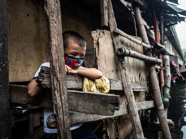 A boy wearing a face mask peeks out of a house located under a bridge in Manila, Philippin