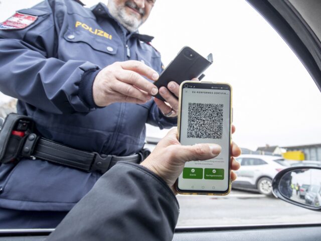 An Austrian police officer checks a driver's digital vaccination certificate on a smartpho