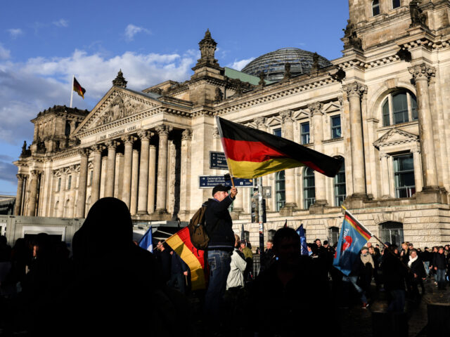 BERLIN, GERMANY - OCTOBER 08: A man waves the German flag as people march in front of the Reichstag to protest against the rising cost of living in a demonstration organized by the right-wing Alternative for Germany (AfD) political party on October 8, 2022 in Berlin, Germany. Consequences stemming from …