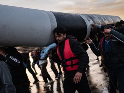 TOPSHOT - Migrants carry a smuggling boat on their shoulders as they prepare to embark on the beach of Gravelines, near Dunkirk, northern France on October 12, 2022, in a attempt to cross the English Channel. (Photo by Sameer Al-DOUMY / AFP) (Photo by SAMEER AL-DOUMY/AFP via Getty Images)