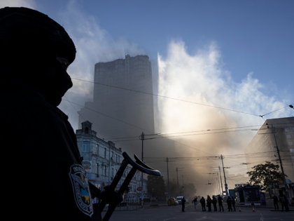 A member of the Ukrainian police force stands guard next to smoke as Kyiv is rocked by explosions during a drone attack in the early morning on October 17, 2022 in Kyiv, Ukraine. The explosions, which authorities reported were caused by “kamikaze drones”, came a week after Russian missile strikes …