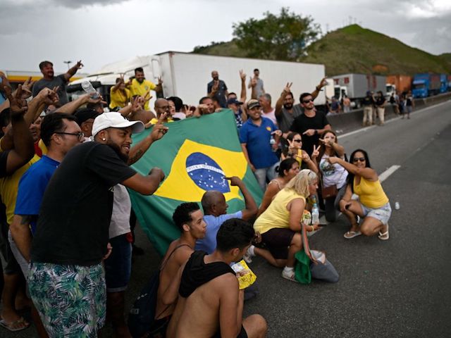 Supporters of President Jair Bolsonaro display a Brazilian national flag as they pose for a picture during a blockade on the Via Dutra BR-116 highway between Rio de Janeiro and Sao Paulo, in Barra Mansa in the Brazilian state of Rio de Janeiro, on October 31, 2022, as an apparent protest, mainly by truck drivers, over Bolsonaro's defeat in the presidential run-off election. - Truckers and other protesters on Monday blocked some highways in Brazil in an apparent protest over the electoral defeat of Bolsonaro to leftist Luiz Inacio Lula da Silva, authorities said. (Photo by Mauro PIMENTEL / AFP) (Photo by MAURO PIMENTEL/AFP via Getty Images)