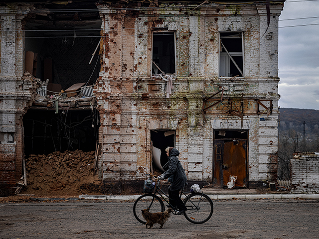 A woman rides a bicycle past a damaged building in the town of Kupiansk on November 3, 2022, Kharkiv region, amid the Russian invasion of Ukraine. (Photo by Dimitar DILKOFF / AFP) (Photo by DIMITAR DILKOFF/AFP via Getty Images)