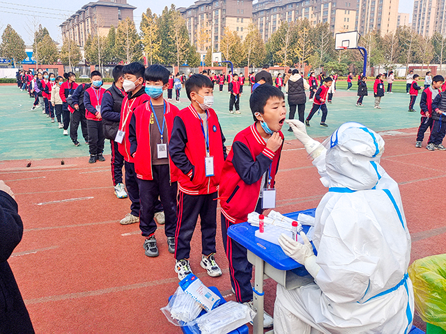 Primary school students line up at a playground for nucleic acid testing in Anyang, Henan