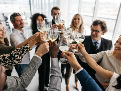 A photo of co-workers giving a toast with champagne in a bright office. They are smartly dressed and have a great time. Horizontal daylight indoor photo.
