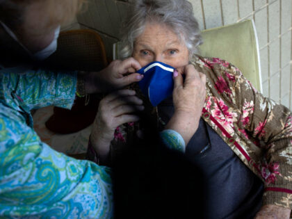 SARASOTA, FLORIDA - JANUARY 7: An 87 year old woman, living in an assisted living facility, is helped by a health care aid in putting on a mask during ta surge in COVID-19 cases, January 7, 2022 in Sarasota, Florida. (Photo by Andrew Lichtenstein/Corbis via Getty Images)