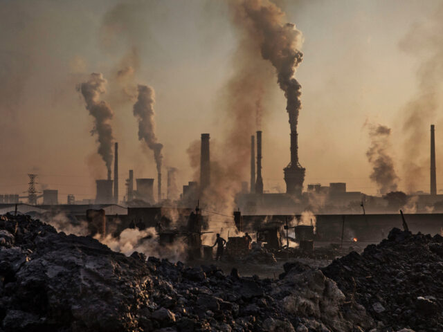 INNER MONGOLIA, CHINA - NOVEMBER 04: Smoke billows from a large steel plant as a Chinese labourer works at an unauthorized steel factory, foreground, on November 4, 2016 in Inner Mongolia, China. To meet China's targets to slash emissions of carbon dioxide, authorities are pushing to shut down privately owned …