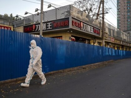 BEIJING, CHINA - NOVEMBER 13: An epidemic control worker wears protective equipment as he walks by a barrier fence in the street in an area where communities have been recently locked down or under health monitoring after COVID-19 cases were recently discovered, on November 13, 2022 in Beijing, China. Though …