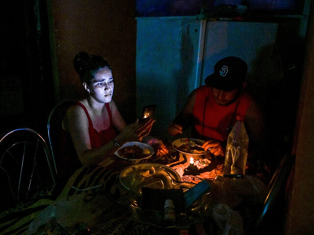 TOPSHOT - A woman looks at her cell phone while eating next to a man by the light of a can