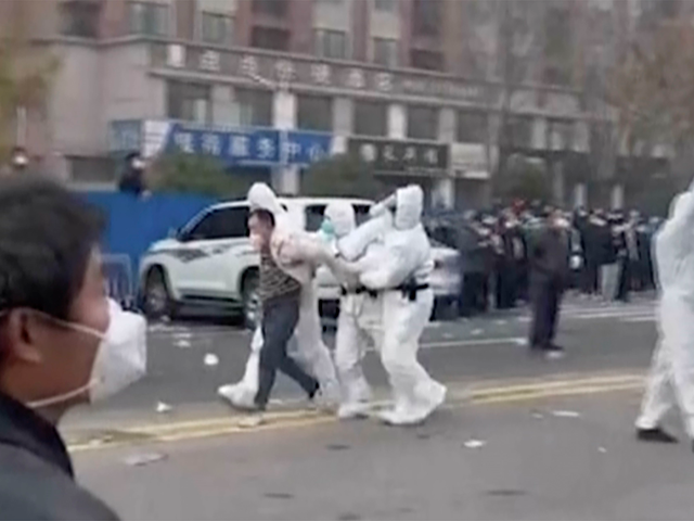 In this photo provided on November 23, 2022, security guards wearing protective clothing are seen leading a person away during a protest at the compound of the factory operated by Foxconn Technology Group, which leads the world's largest Apple iPhone factory in Zhengzhou, Henan Province, central China.  Workers at the world's largest iPhone factory were beaten and detained during protests over wages amid virus checks, witnesses and social media videos show on Wednesday, as tensions mount about Chinese efforts to combat a further rise in infections.  (AP)