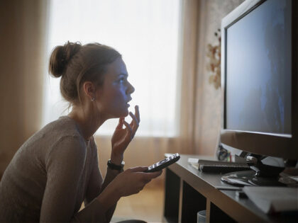 Young woman looking in suspense at tv - stock photo