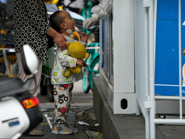 A child holding a soft toy gets a throat swab at a COVID-19 testing facility in Beijing, M