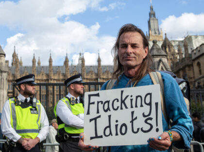 An environmental climate campaigner stands outside Parliament with an anti-fracking sign d