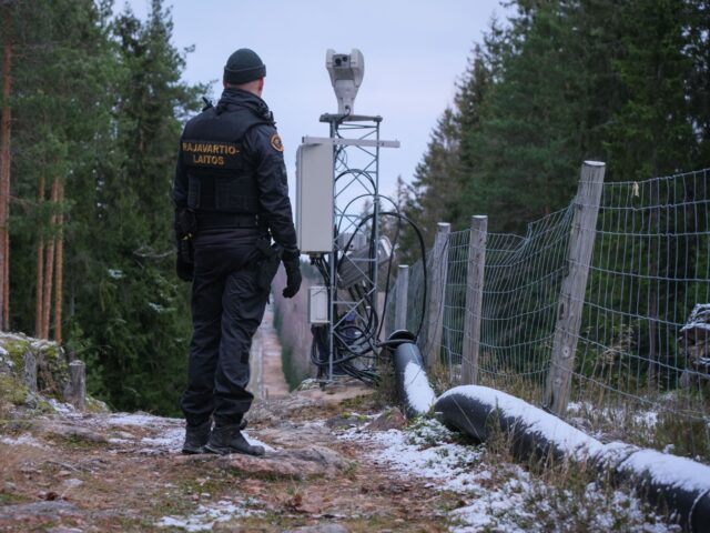 Senior border guard officer Juho Pellinen stands along a fence marking the boundary betwee