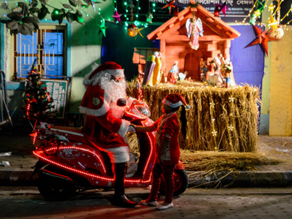 A man dressed as Santa Clause is seen on a scooter as he shakes hand with a little girl in front of a nativity scene ahead of Christmas in Kolkata , India , on 22 December 2022 . (Photo by Debarchan Chatterjee/NurPhoto via Getty Images)