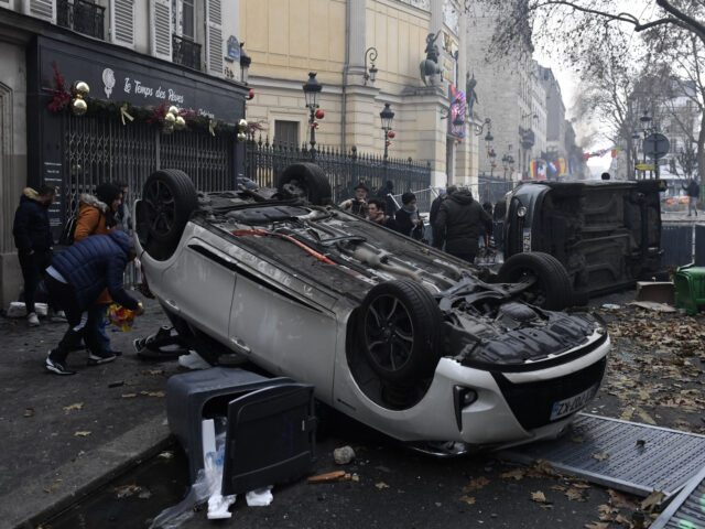 People pass by cars which have been turned over during clashes following a demonstration of members of the Kurdish community, a day after a gunman opened fire at a Kurdish cultural centre killing three people, at The Place de la Republique in Paris on December 24, 2022. - The shots …