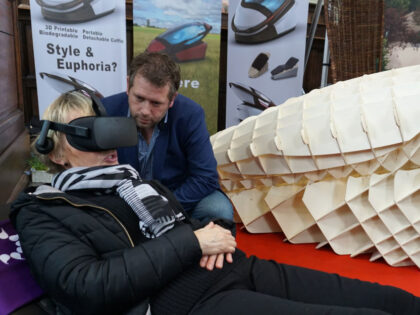 Dutch designer Alexander Bannink explains how the "Sarco" euthanasia pod works as a woman experiences sitting in the device by wearing virtual reality glasses, on April 14, 2018 at the Amsterdam Funeral Expo. Called the "Sarco", short for sarcophagus, the 3D-printed machine invented by Australian euthanasia activist Philip Nitschke and …