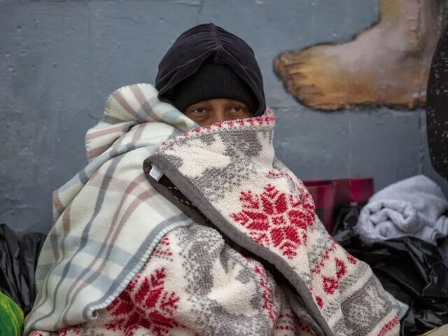 A migrant covers himself with blankets while waiting for help in downtown El Paso, Texas, Sunday, Dec. 18, 2022. (AP Photo/Andres Leighton)
