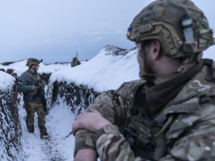 Ukrainian servicemen walk along a snow-covered trench guarding their position at the front