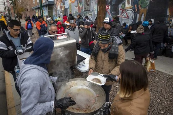 Local volunteers serve warm food to the migrants camping out on the streets of El Paso. (AP Photo/Andres Leighton)