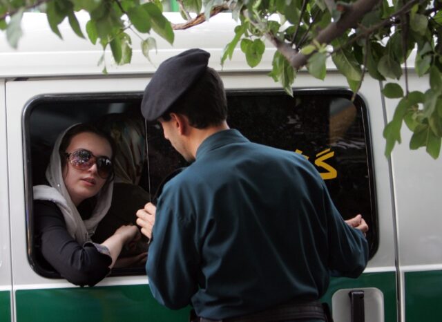 An Iranian officer (R) speaks with a woman arrested for wearing 'inappropriate' clothes in