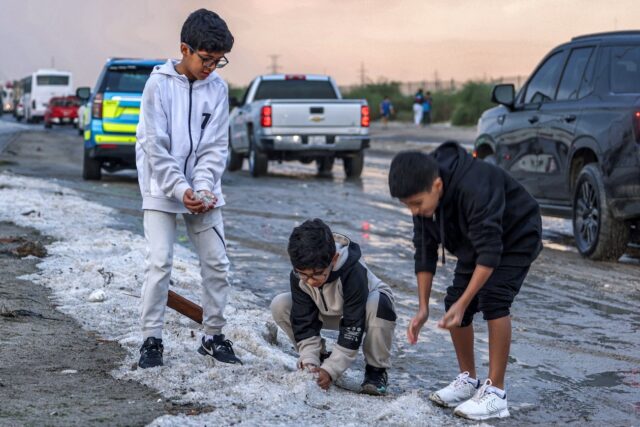 Children toss handfuls of hail after a winter storm in the Umm al-Haiman district south of