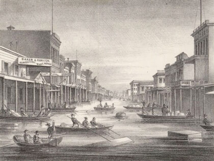 J street in downtown Sacramento seen from levee showing flood of 1862; people in boats make their way between buildings in flooded city streets. (Wikimedia Commons)