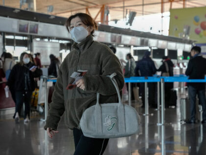 A woman wearing a face mask walks by travelers with luggage line up at the Air Macao fligh