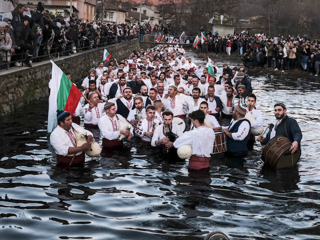 Men play bagpipes and drums as they form a procession into the cold Tundzha River to celebrate Epiphany in the town of Kalofer, Friday, Jan. 6, 2023. The legend goes that the person who retrieves the wooden cross will be freed from evil spirits and will be healthy throughout the year. After the cross is fished out, the priest delivers a special blessing to that man and his household. In the small mountain city of Kalofer in central Bulgaria the ritual lasts longer, as nearly a hundred men dressed in traditional white embroidered shirts wade into the Tundzha River to perform a slow men's dance. (AP Photo/Alexander Nikolov)