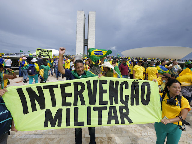 Protesters, supporters of Brazil's former President Jair Bolsonaro, hold a banner that reads in Portuguese " Military Intervention" as they storm the the National Congress building in Brasilia, Brazil, Sunday, Jan. 8, 2023. (AP Photo/Eraldo Peres)
