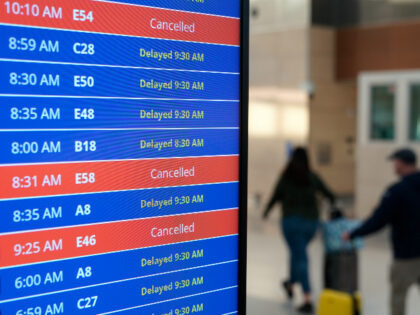 Travelers walk as a video board shows flight delays and cancellations at Ronald Reagan Washington National Airport in Arlington, Va., Wednesday, Jan. 11, 2023. (AP Photo/Patrick Semansky)