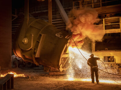 Steelworker cleaning pouring end of flask during steel pour in steelworks