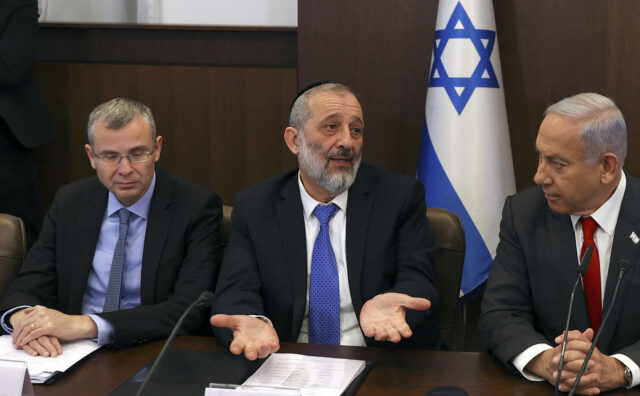 Israel's Interior and Health Minister Aryeh Deri (C) reacts as he sits between Prime Minis