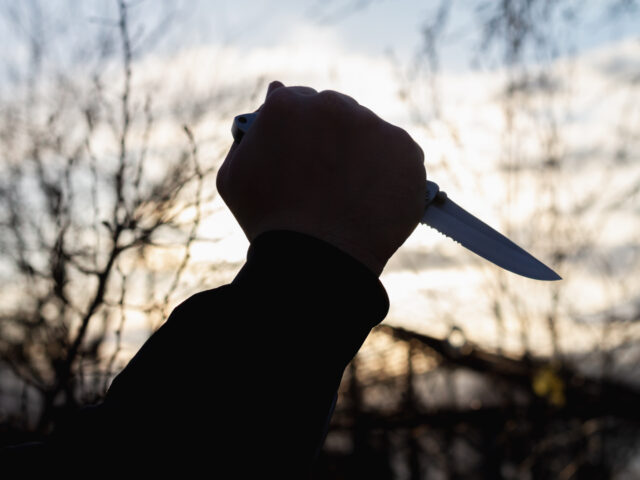 A knife in the hand of a man with a sharp steel blade in the park as a weapon or a means o