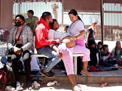 SAN LUIS, ARIZONA - MAY 21: A pregnant immigrant from Haiti is assisted by her partner (left, center) and another immigrant while having contractions after she crossed from Mexico, with the U.S.-Mexico border barrier in the background, on May 21, 2022 in San Luis, Arizona. A U.S. Border Patrol agent …