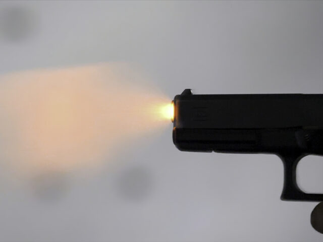 Close profile of man holding a 9 mm handgun, then takes a shot. Man fires hand gun at indo