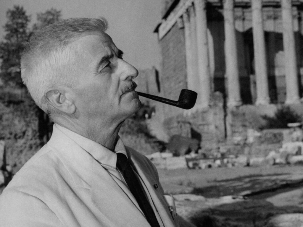 American writer William Faulkner (William Falkner) smoking the pipe beside an archaeological site. Rome, September 1955. (Photo by Mondadori via Getty Images)