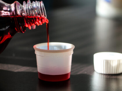 Close-Up Of Bottle Pouring Cough Syrup In Container On Table - stock photo