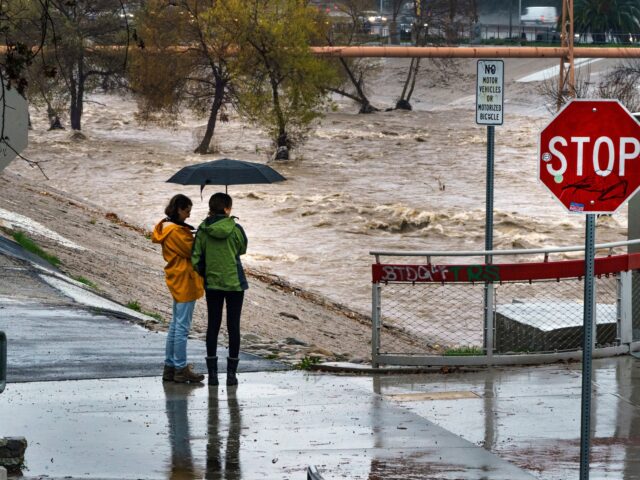 People watch the high volume of storm rain water flowing downstream at the Los Angeles Riv