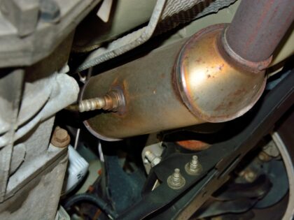 Selective focus on a stainless steel catalytic converter with an oxygen sensor or O2 sensor installed on an exhaust system under a vehicle. Catalytic converters have become a target for theft.